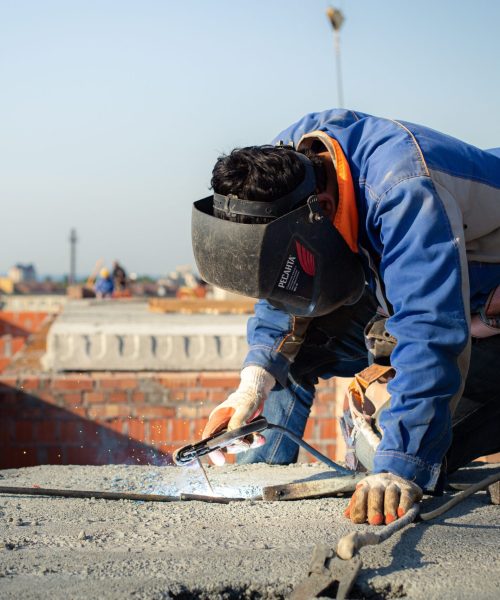 Focused welder in protective gear welding on a city rooftop construction site.