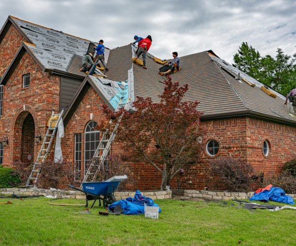 Roofers working on brick home in Allen, Texas, addressing shingles and roofing materials.