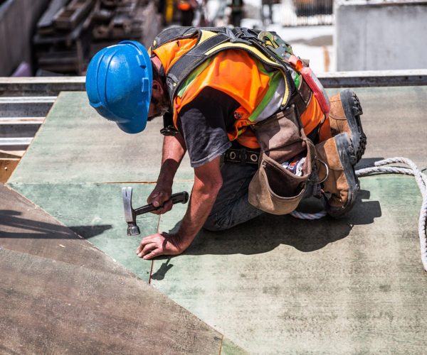 A skilled construction worker in protective gear hammering a rooftop panel.